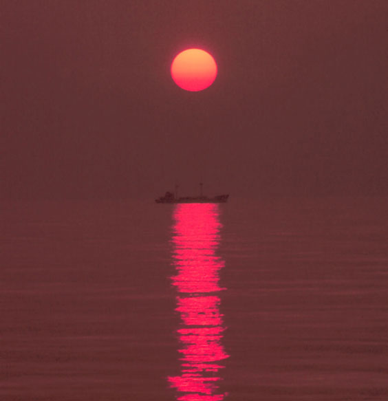 A small coastal freighter plying its way through a placid sea at sunset. Photo by Commander John Bortniak, NOAA Corps (r