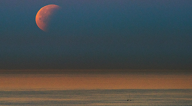 A sailboat floats near the eastern cliffs of Navy Base Point Loma, California in view of the first super blue blood moon