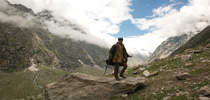 An old man standing on a rock up in the mountains